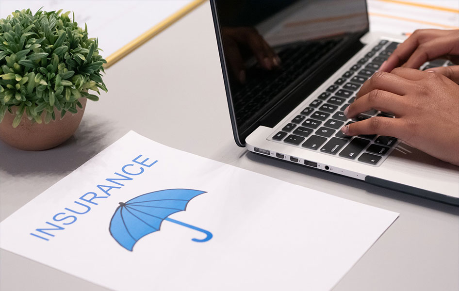 Paper with travel insurance and umbrella print, beside laptop where a person is typing