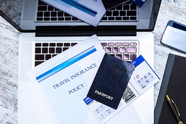 travel insurance policy, passport and airline ticket or boarding pass on top of a laptop